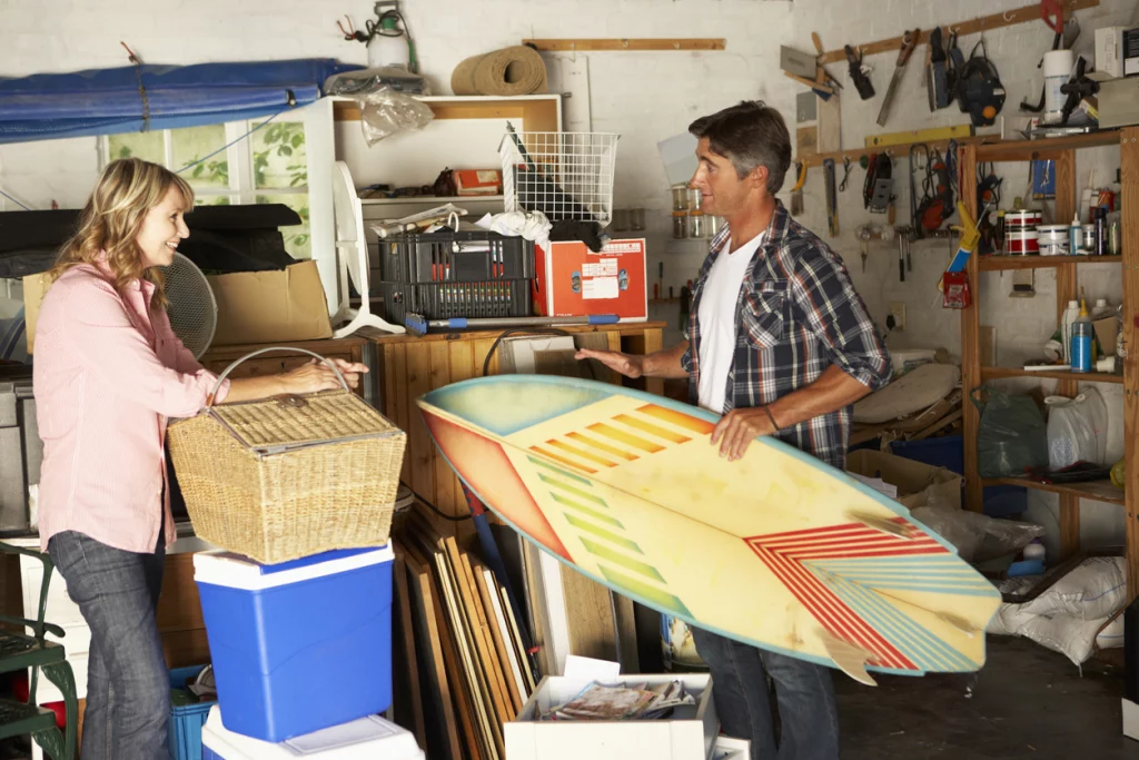 Couple Clearing Garage For Yard Sale Discussing Surf Board
